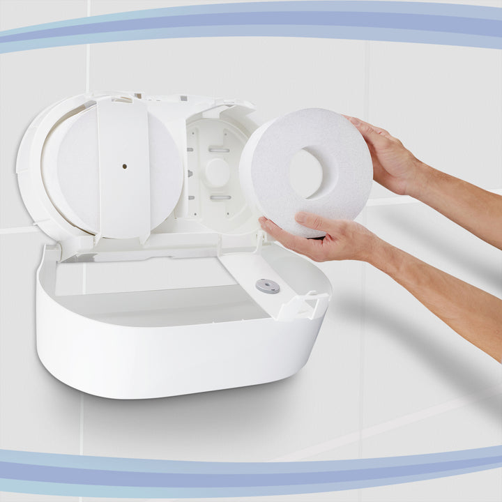 Hands loading a roll into a white AQUARIUS twin roll centrepull toilet paper dispenser mounted on a tiled wall, showing open mechanism and hygienic design
